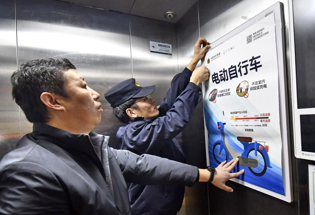 安全生产检查人员在北京市大兴区天宫院街道的居民楼电梯内张贴电动自行车安全使用宣传画。新华社记者李欣 摄