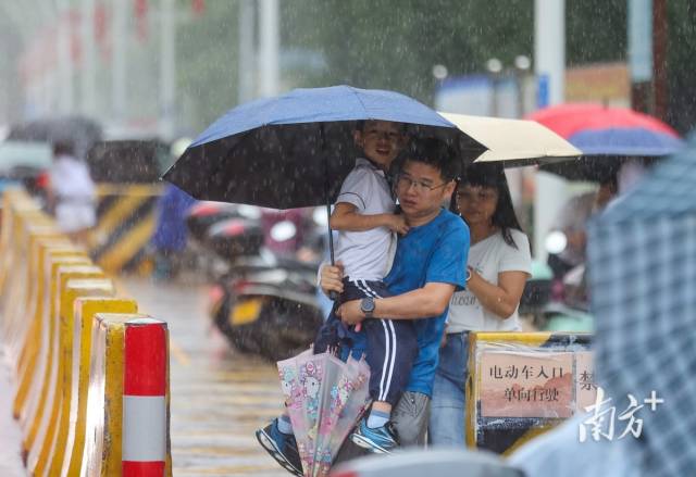 南区街道情景路,暴雨中家长抱着小孩走向车子。